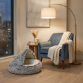 Grey plush cat cave bed beside a blue velvet armchair with city night view